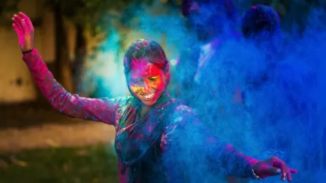Young woman dancing around a cloud of color powder while celebrating the indian Holi day