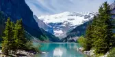 Beautiful Lake Louise with Victoria Glacier in the background and a glistening emerald lake. Several canoes can be seen at a distance on the lake.