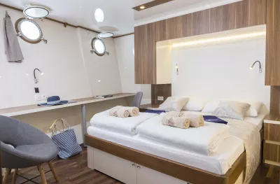 Double bed cabin with white decor with clean rolled and folded towels placed on the end of the made bed 