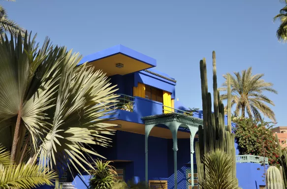 Vibrant yellow and blue house, with palm trees in front of it in Marrakech