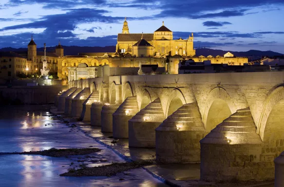 Roman Bridge on the Guadalquivir River and Mosque Cathedral, illuminated at dusk in Cordoba, Spain.