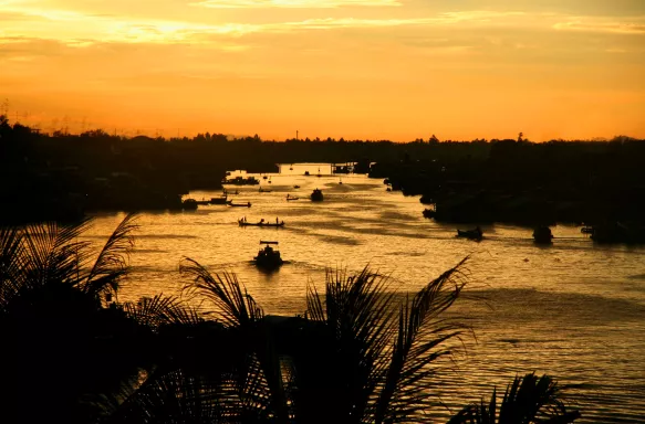 Sunset skies over Mekong River with silhouettes of tree and boats visible along the water