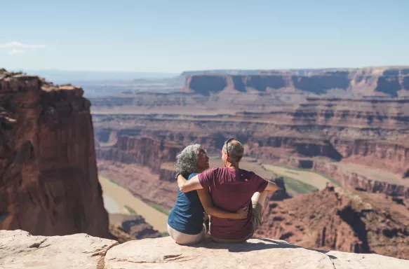 An mature couple sitting atop a canyon cliff edge, overlooking the valley below in Utah
