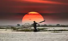 Vietnamese fisherman on his boat during sunset, balancing a oar paddle