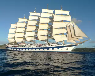 Exterior side shot of the white and blue Royal Clipper ship with tall sails cruising the ocean