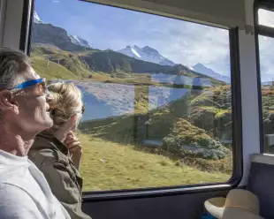 Mature couple in moving train enjoying the passing view of the Swiss alps and alpine area.