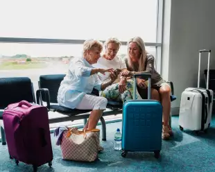 Three mature women in an airport waiting area with their suitcases and phones