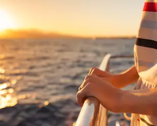 Close-up of hands holding onto rail on a yacht during sunset