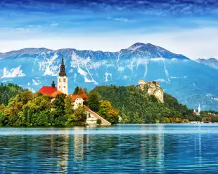 Church on the Island and ancient castle on top of a rock with European Alps in background at Lake Bled, Slovenia