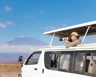 Professional photographer taking shots of Kilimanjaro mount aboard safari jeep, Kenya, Africa.