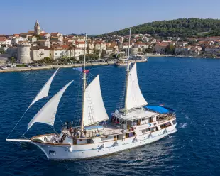 MS Mendula sailing with sails up, coastline in the background