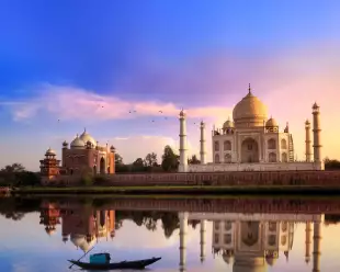 View of the Taj Mahal at sunset, it's image reflected in the water of a foreground lake.