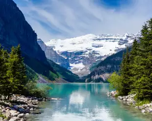 Beautiful Lake Louise with Victoria Glacier in the background and a glistening emerald lake. Several canoes can be seen at a distance on the lake.