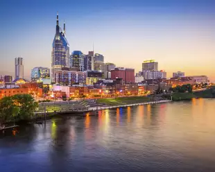 Nashville downtown skyline before sunset along a clear sky, it's reflection displayed in the foreground of the Cumberland River.