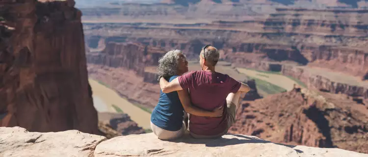 An mature couple sitting atop a canyon cliff edge, overlooking the valley below in Utah