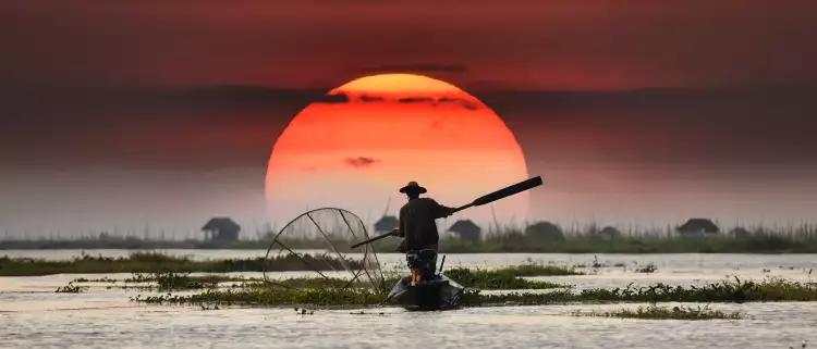 Vietnamese fisherman on his boat during sunset, balancing a oar paddle