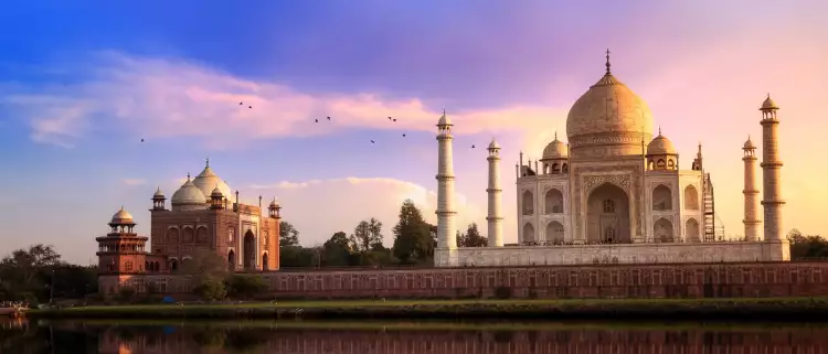 View of the Taj Mahal at sunset, it's image reflected in the water of a foreground lake.