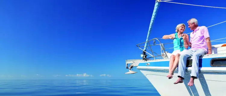 Happy senior couple sitting on the bow of a sail boat on a calm blue sea